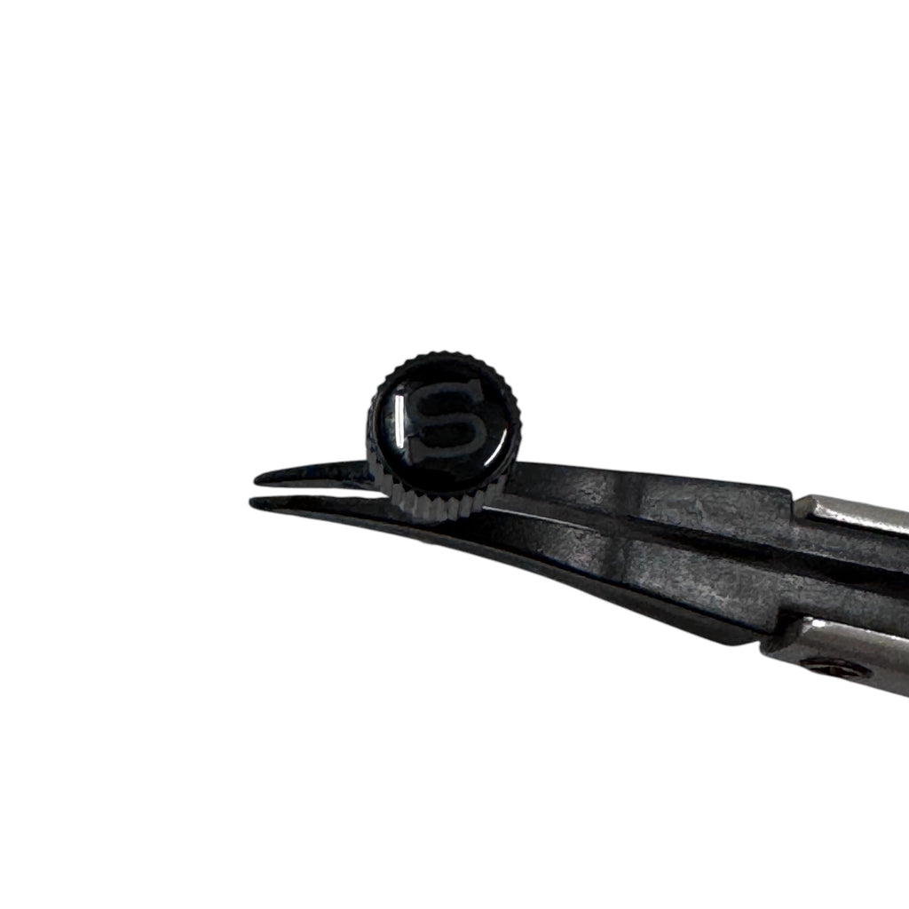 A polished black coin-edged screw-down crown for a watch, held by a pair of tweezers against a white background, top view