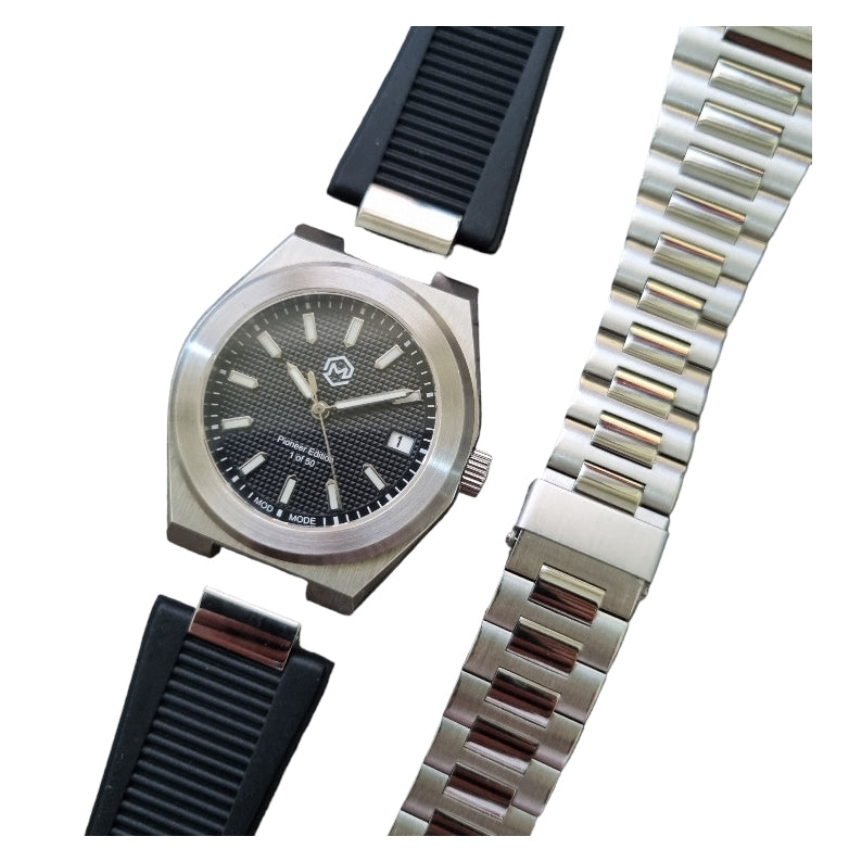 A silver-toned Project MM1 Pioneer Edition watch with a black waffle dial, stainless steel bracelet, and a vulcanised rubber strap.